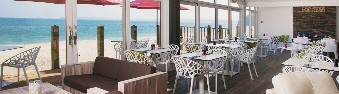 Landscape of beach club restaurant with white chairs and tables overlooking beach.