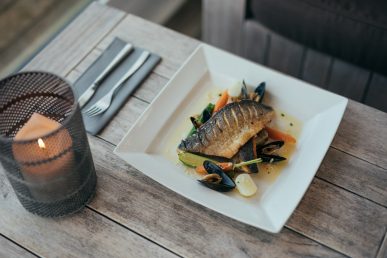 Square plate of fish laid up on table with candle.