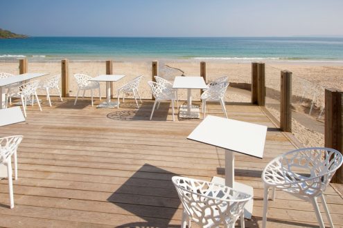 Tables and chairs on wooden decking with beach behind.