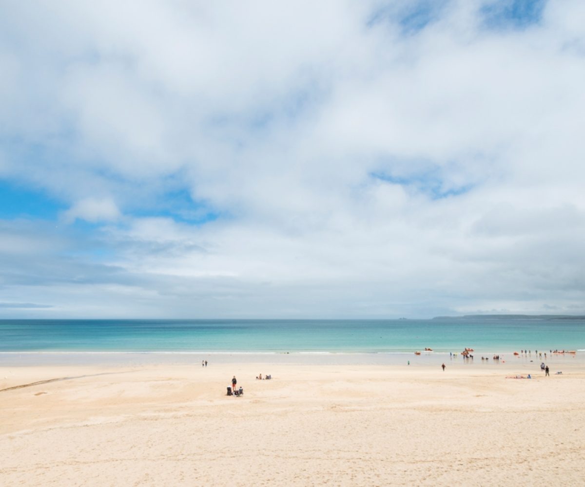Carbis Bay beach with lightly cloudy sky.