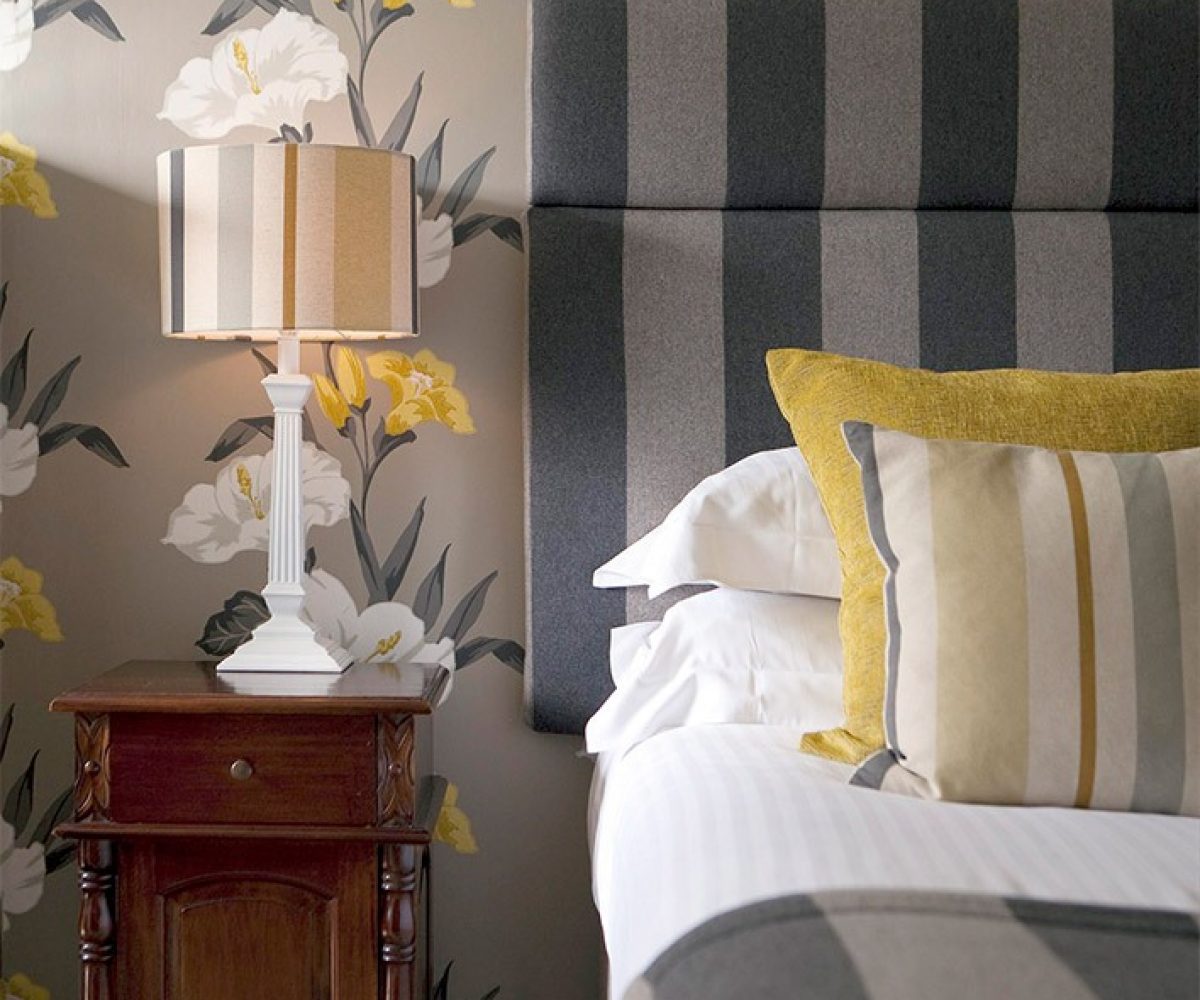 Bed with striped headboard against bold floral wallpaper.