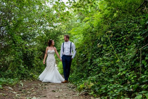 Bride and groom walking in woodland.