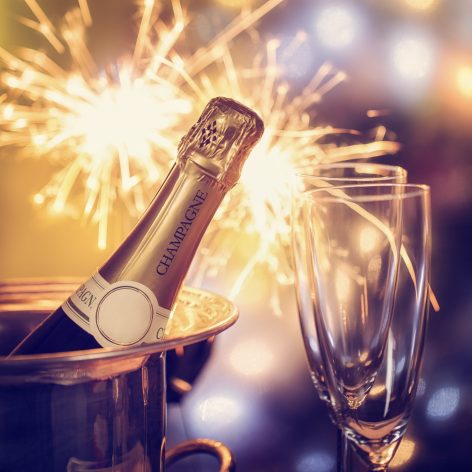 Unopened champagne bottle with glasses and sparkler in background.