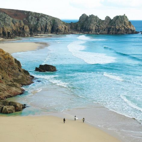 Three people walking along beach next to cliffs